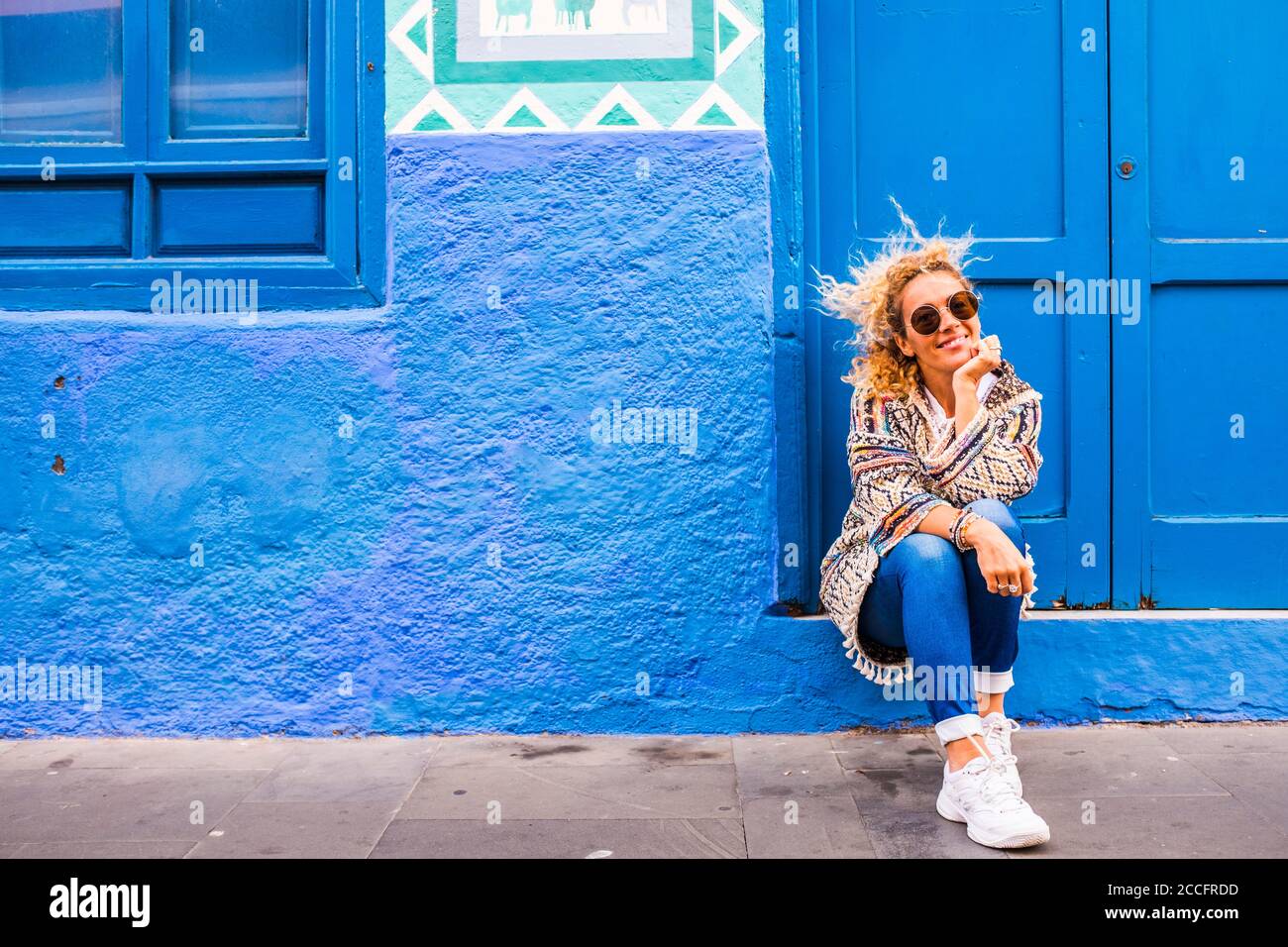 Chererful e rilassata bella donna sedersi fuori una colorata blu casa in strada - la gente proprietario di proprietà della casa concetto - stile di vita di viaggio a Foto Stock