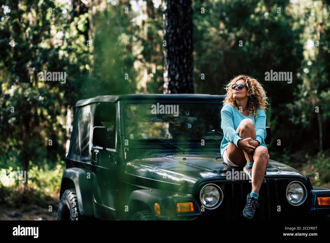 Bella donna siede donw sulla macchina fuori strada e. godetevi la natura intorno - concetto di vacanza fuori rete e viaggio con legno e alberi - la gente gode di th Foto Stock