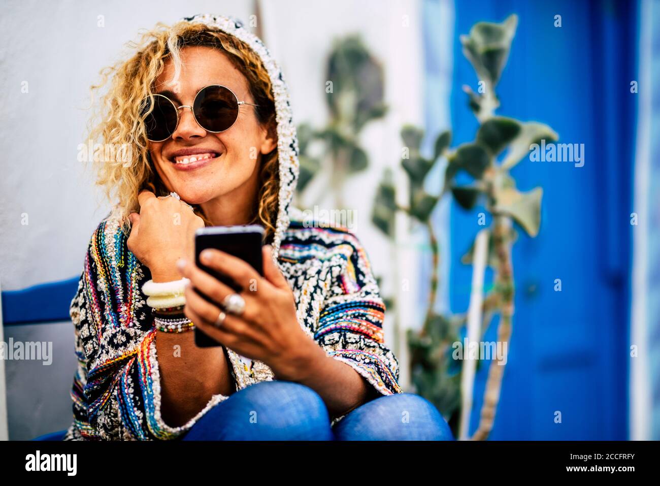 Bella donna usare cellulare e sorridere - la gente godere stagione invernale all'aperto - bella femmina caucasica con occhiali da sole e. giacca alla moda e blu Foto Stock