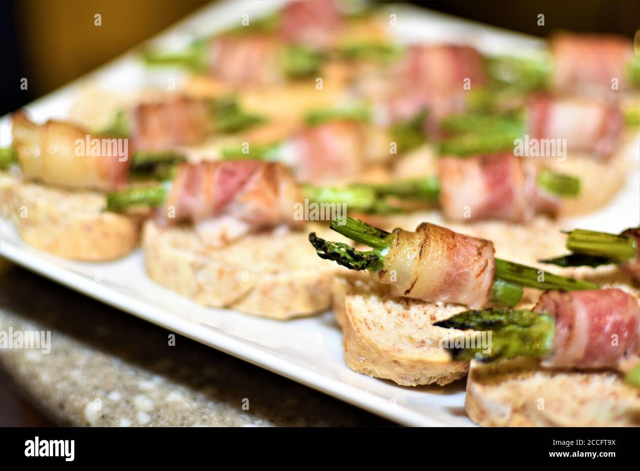 Un piatto di antipasti fatti di spighe di asparagi alla griglia avvolte in pancetta e posto sopra dei piccoli pezzi di pane Foto Stock