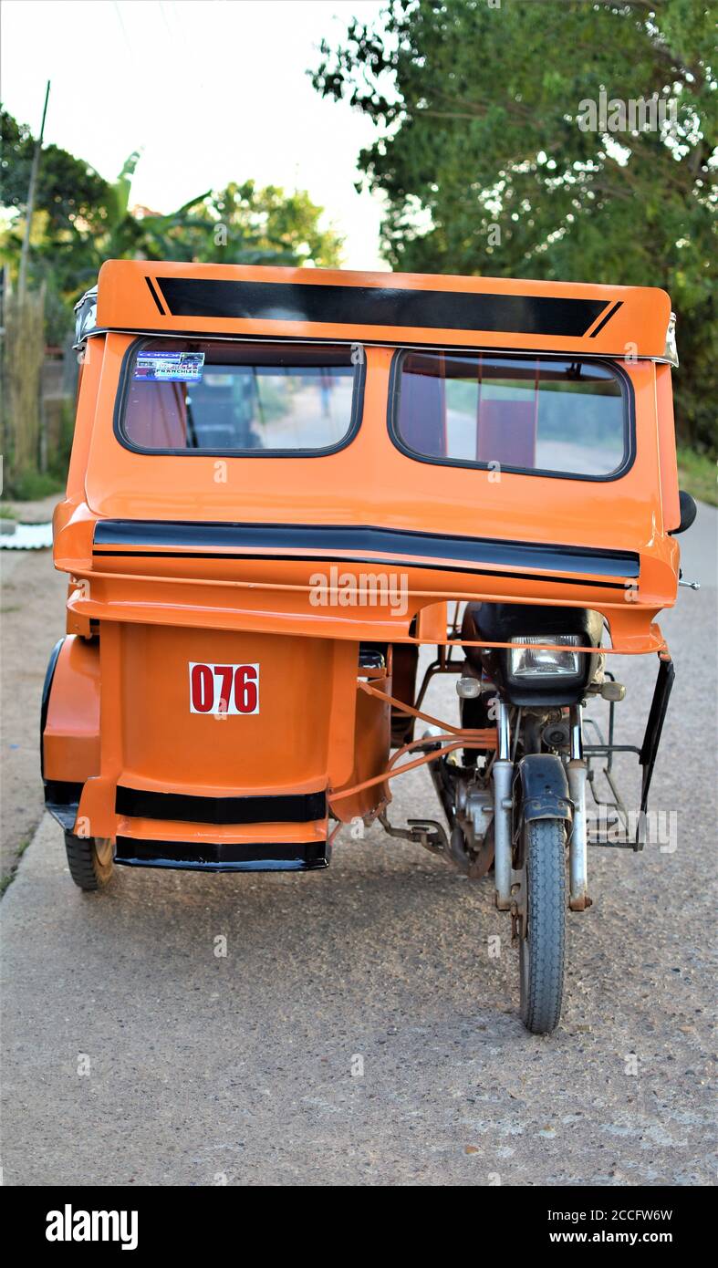 Un triciclo arancione vuoto è parcheggiato sul lato di una strada in cemento a Coron, Palawan Foto Stock