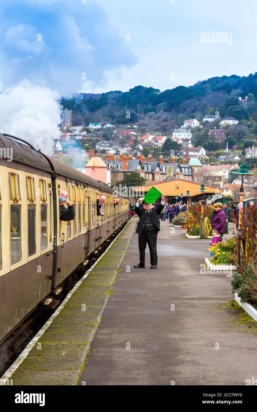 Una guardia lancia la bandiera verde per autorizzare un treno a vapore a partire dalla stazione di Minehead, West Somerset Railway Spring Gala evento, Inghilterra, Regno Unito Foto Stock