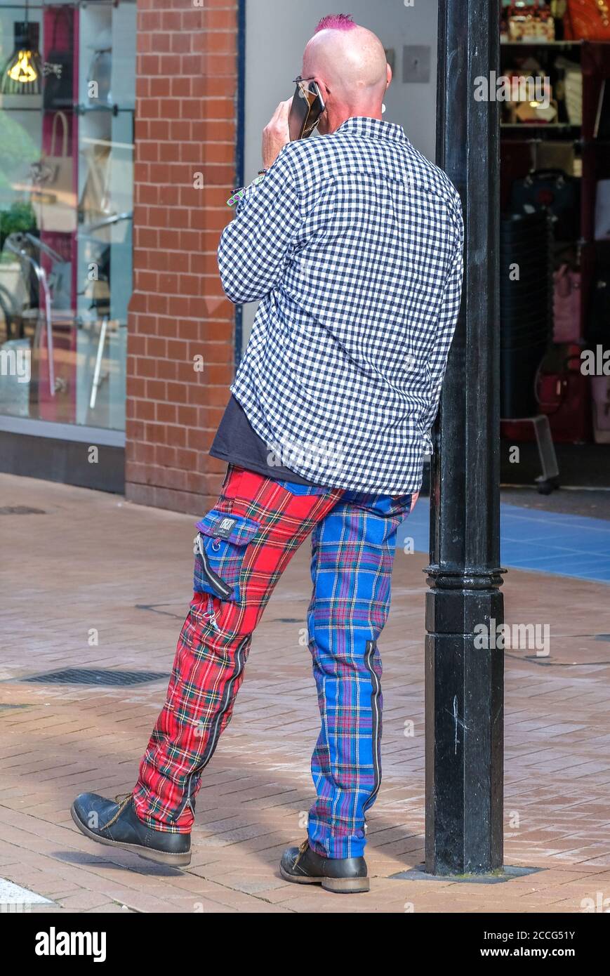 punk appoggiato al palo della lampada e pantaloni blu/rosso con controllo sportivo alternato Foto Stock