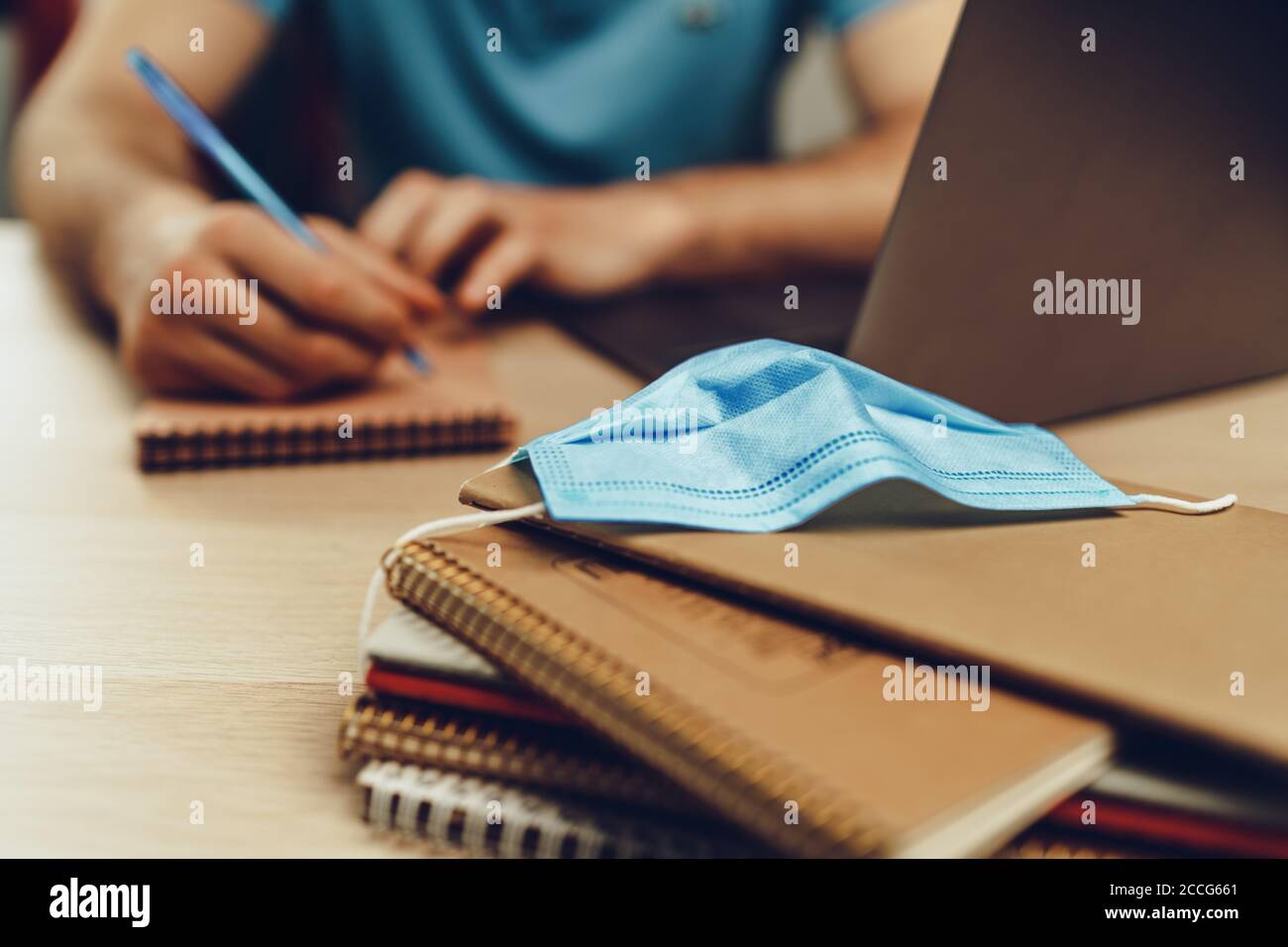 Studentesse maschi a casa durante la quarantena. Primo piano di un tavolo con computer portatile, notebook e maschera medica Foto Stock