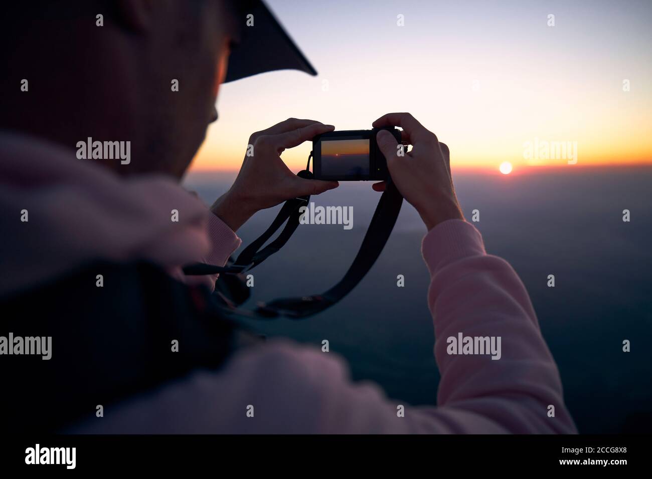 Giovane uomo che tiene la macchina fotografica e che fotografa il sole sotto l'orizzonte. Foto Stock