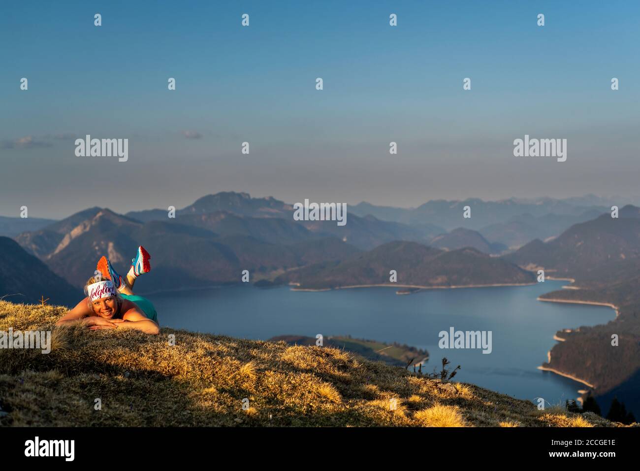 Il corridore del sentiero Katharina Kirschner si trova su un prato di primavera su Simetsberg, sullo sfondo il Walchensee e sorride alla telecamera. Foto Stock