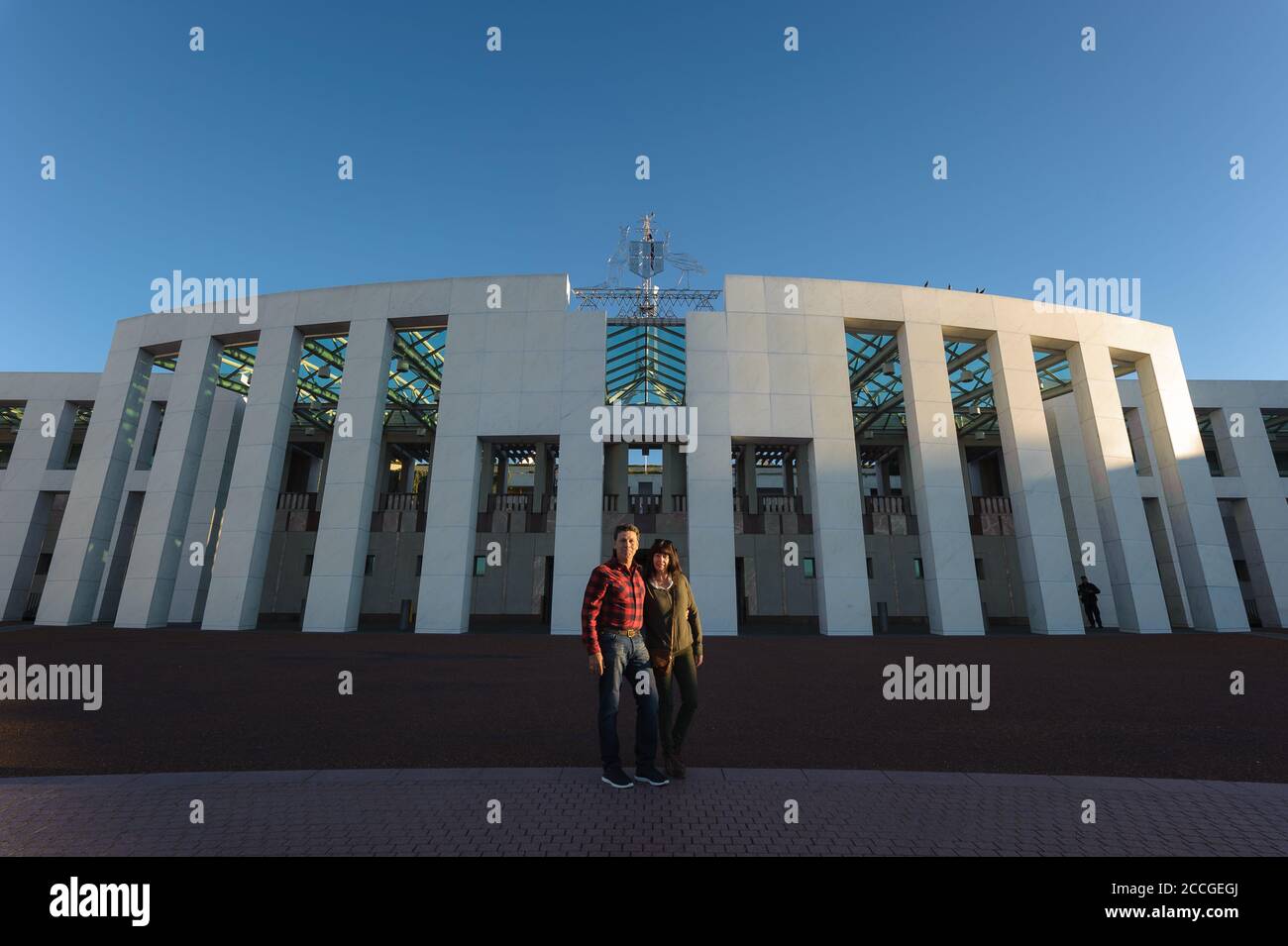 Una coppia turistica che si abbraccia l'una con l'altra in un giorno d'inverno limpido di fronte all'entrata principale della casa del parlamento australiano a Canberra. Foto Stock