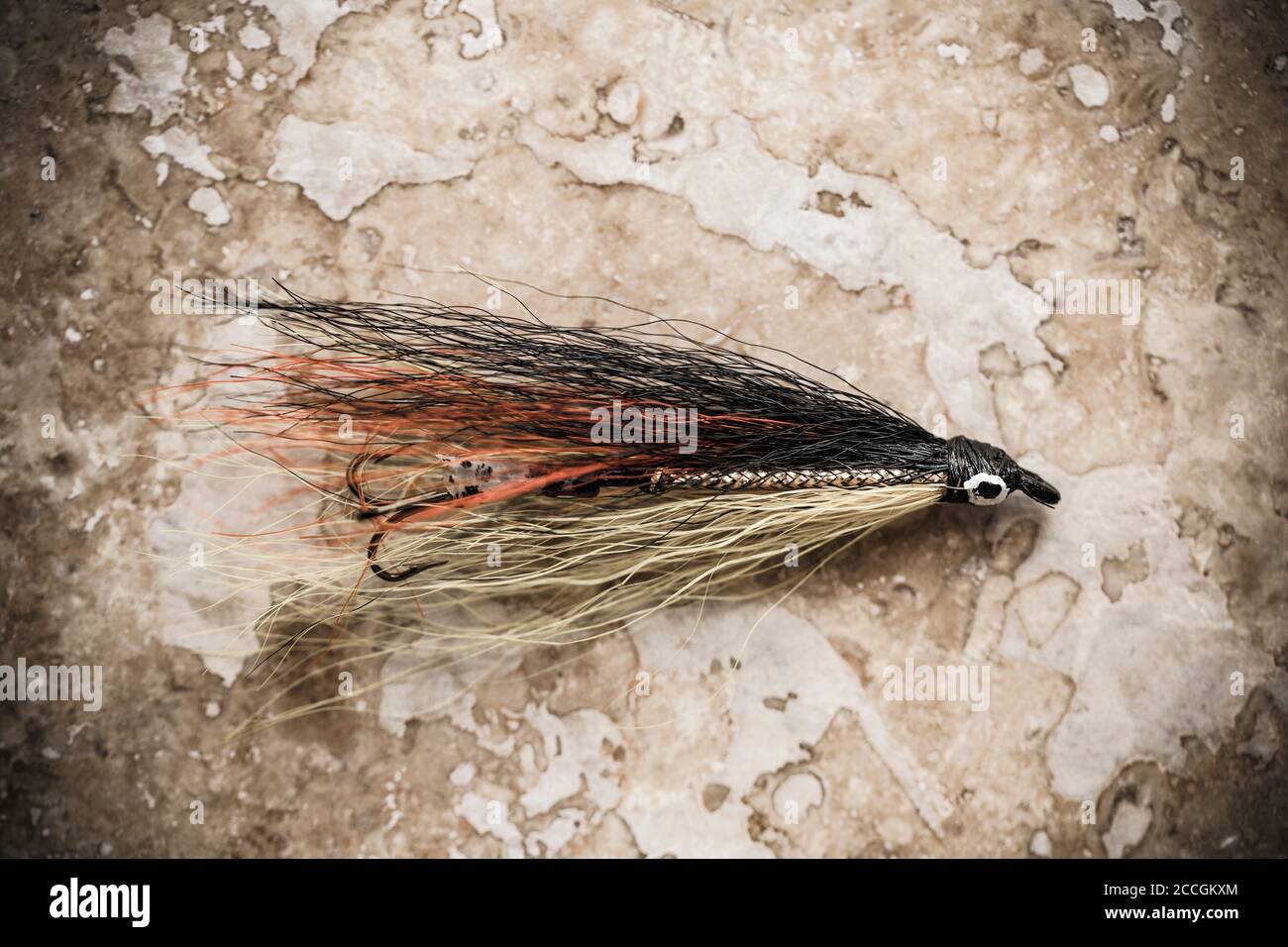 Una vecchia mosca di salmone, forse fatta in casa, da una collezione di attrezzatura da pesca d'annata. Colori desaturati su uno sfondo di pietra chiaro. Dorset Inghilterra Regno Unito Foto Stock