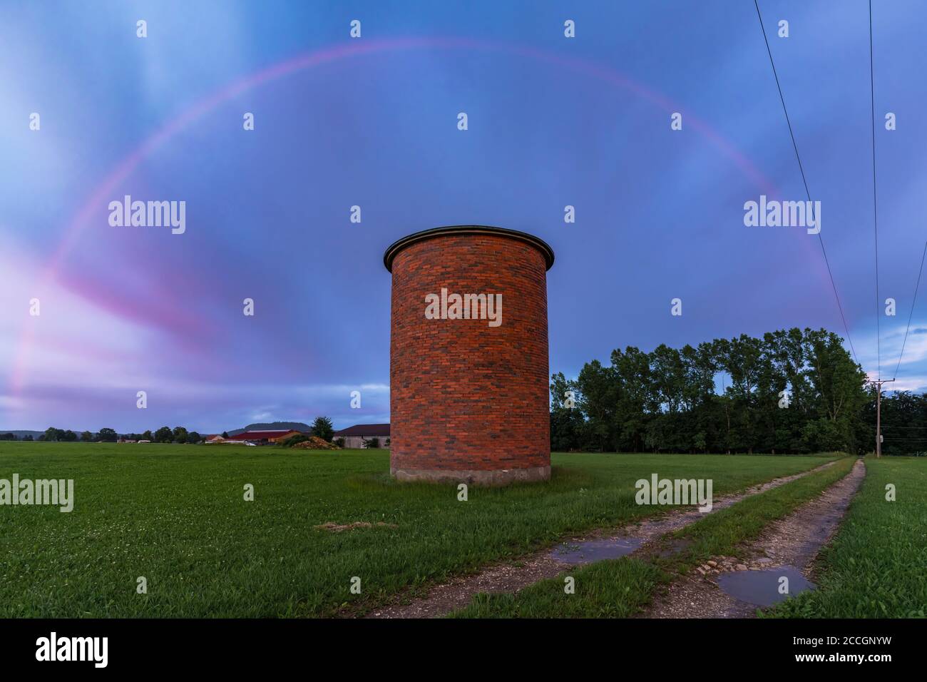 Arcobaleno durante un tramonto con un cielo di colori spettacolari. In primo piano un silo di mattoni. Foto Stock