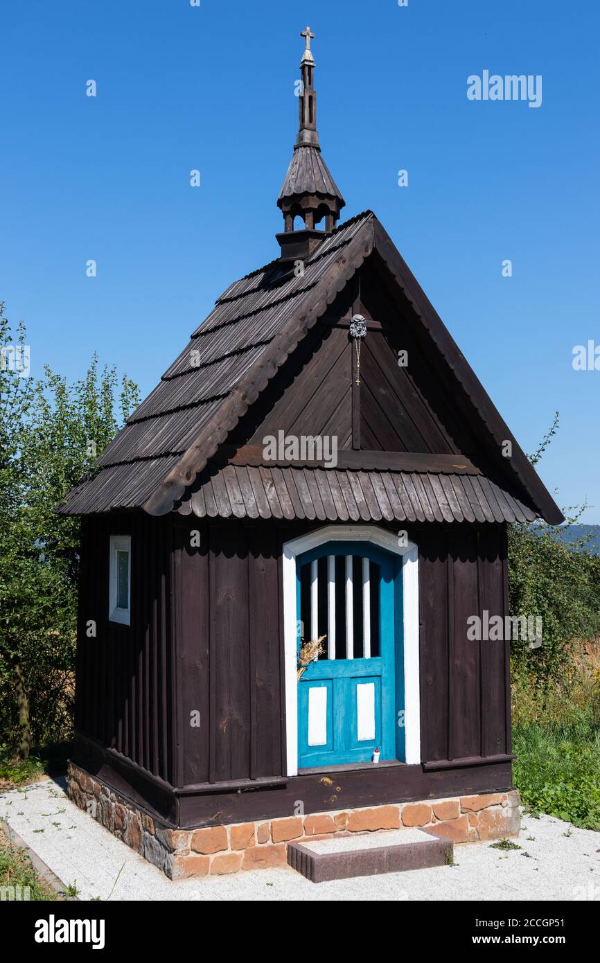 Scatto simmetrico di cappella di legno scuro con porte blu. Polonia intorno a Kielce. Cielo blu e alberi verdi sullo sfondo, nessuna gente. Antico tradizionale Foto Stock