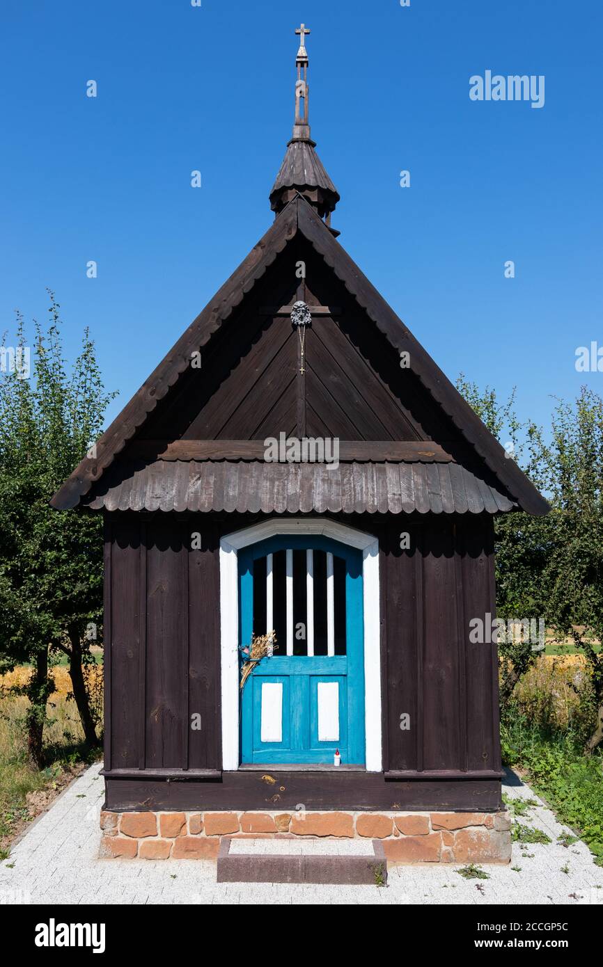 Scatto simmetrico di cappella di legno scuro con porte blu. Polonia intorno a Kielce. Cielo blu e alberi verdi sullo sfondo, nessuna gente. Antico tradizionale Foto Stock