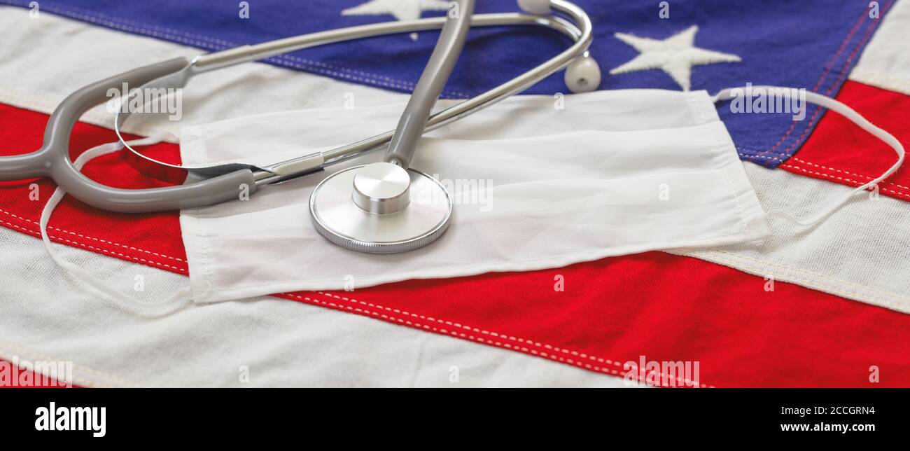USA sanità, giorni di coronavirus. Stetoscopio medico e maschera facciale protettiva su una bandiera degli Stati Uniti d'America, striscione. COVID 19 assicurazione sanitaria americana co Foto Stock