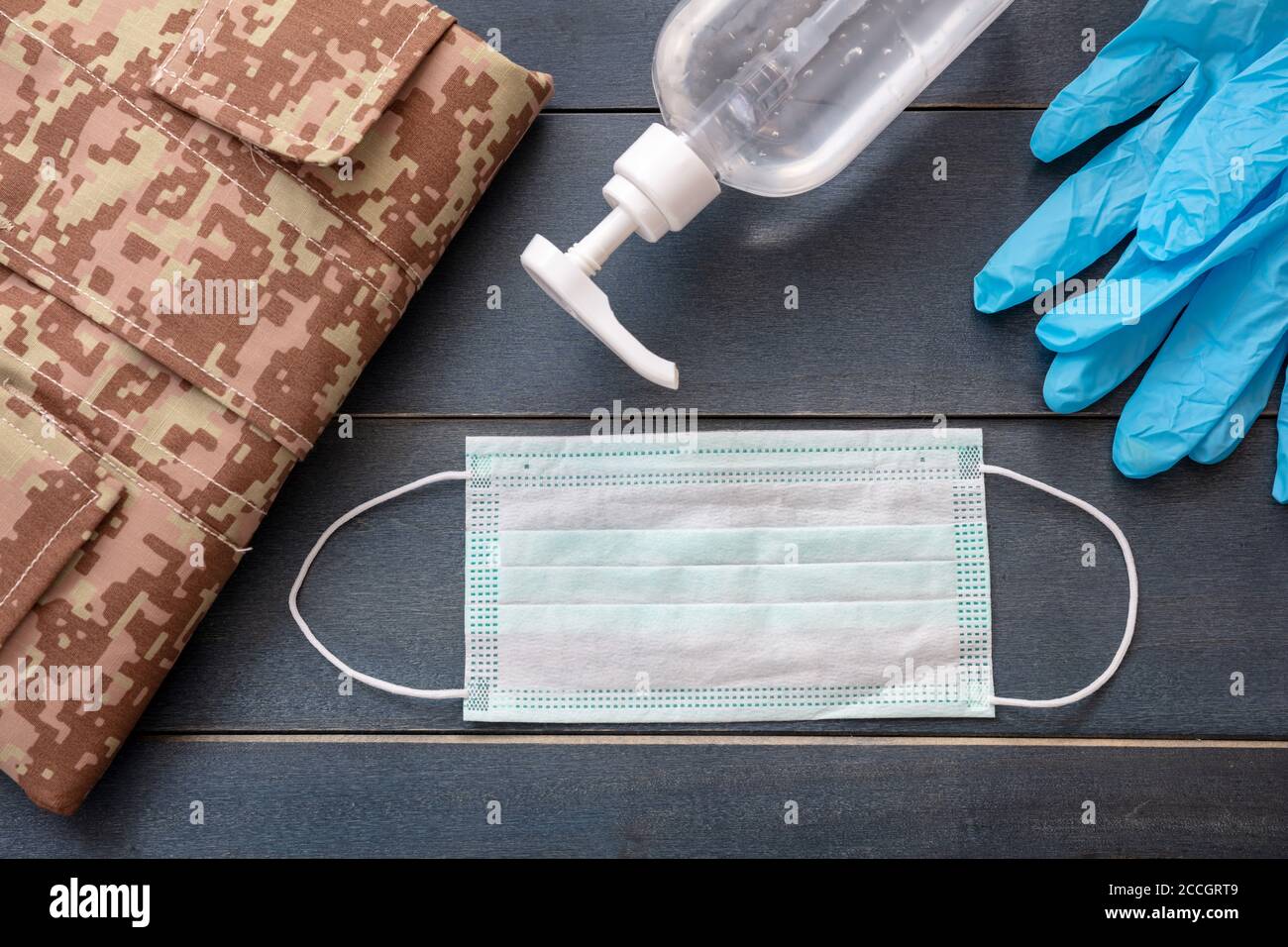 Concetto di protezione del coronavirus dell'esercito. Disinfettante per le mani, guanti protettivi, maschera medica e uniforme dell'esercito statunitense su sfondo di legno di colore blu. Covid Foto Stock