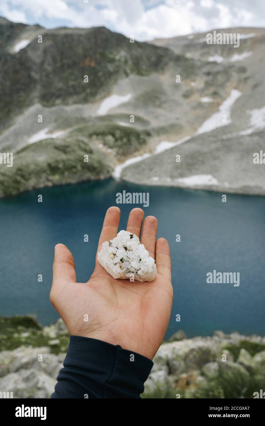 POV colpo di cristallo di roccia in mano mans tra lago di montagna selvaggio. Foto Stock