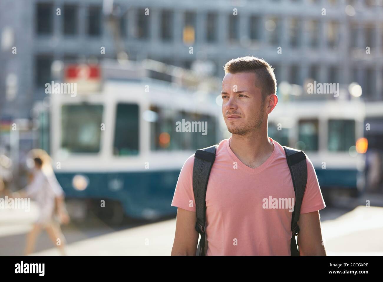 Giovane uomo che cammina sulla trafficata strada della città contro la stazione del tram. Zurigo, Svizzera Foto Stock