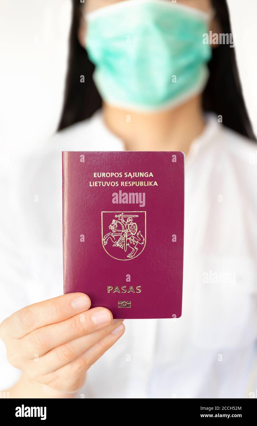 Una donna con una maschera chirurgica che tiene il passaporto lituano durante l'epidemia di Covid 19. Foto Stock