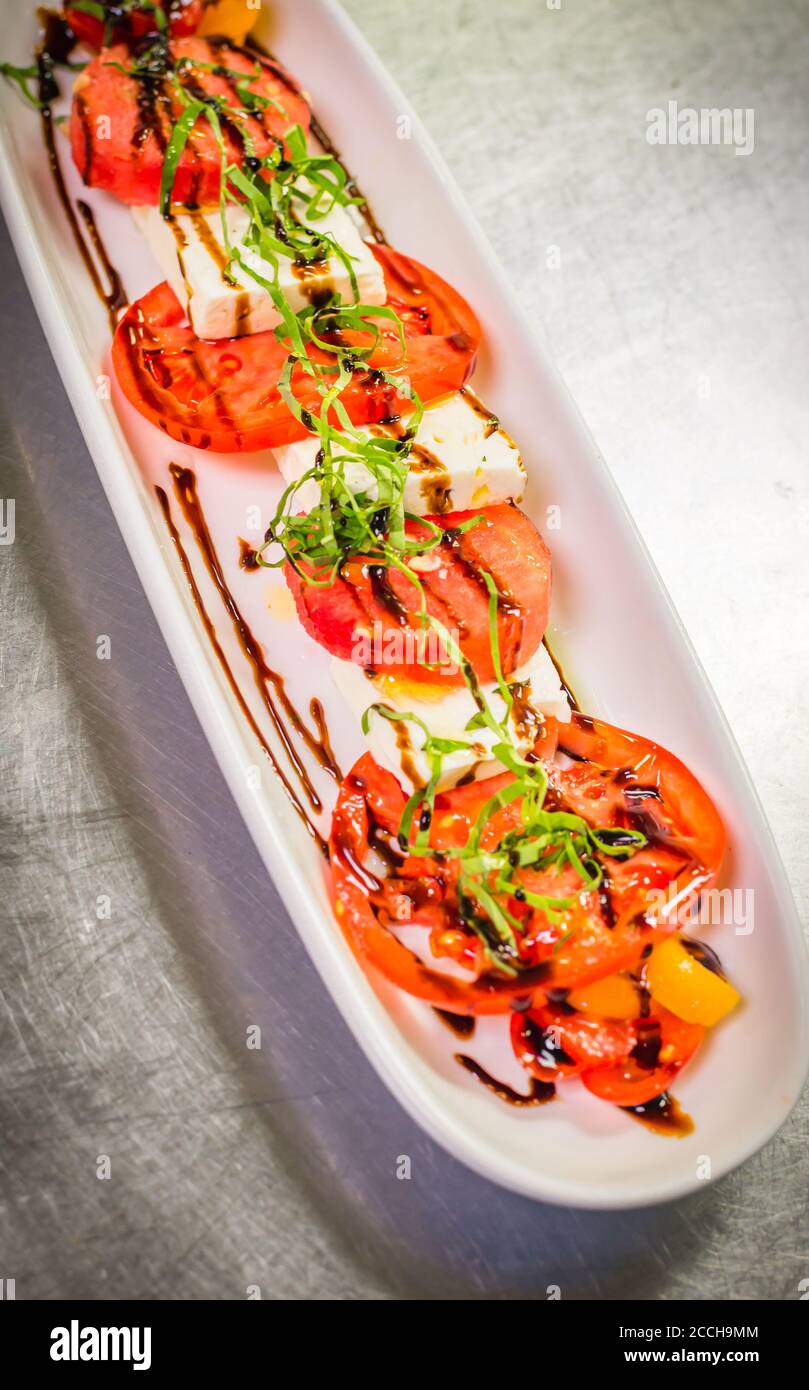 Antipasti di insalata caprese da fattoria a tavola preparati con pomodori freschi, basilico, mozzarella e una riduzione/smalto balsamico Foto Stock