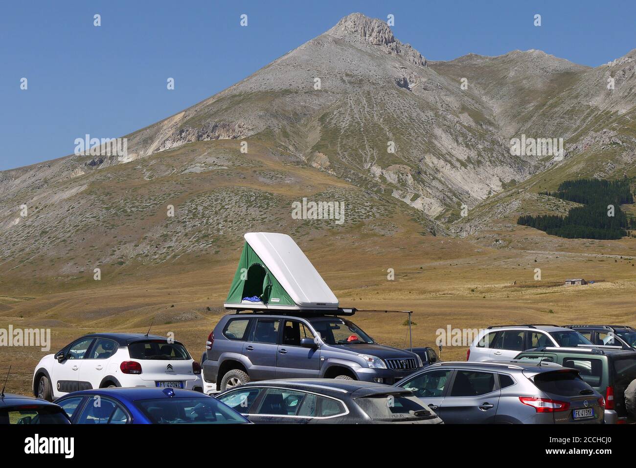 Un'auto con una tenda sul tetto tra veicoli parcheggiati a campo Imperatore nel Gran Sasso D'Italia, Abruzzo, Italia. Foto Stock