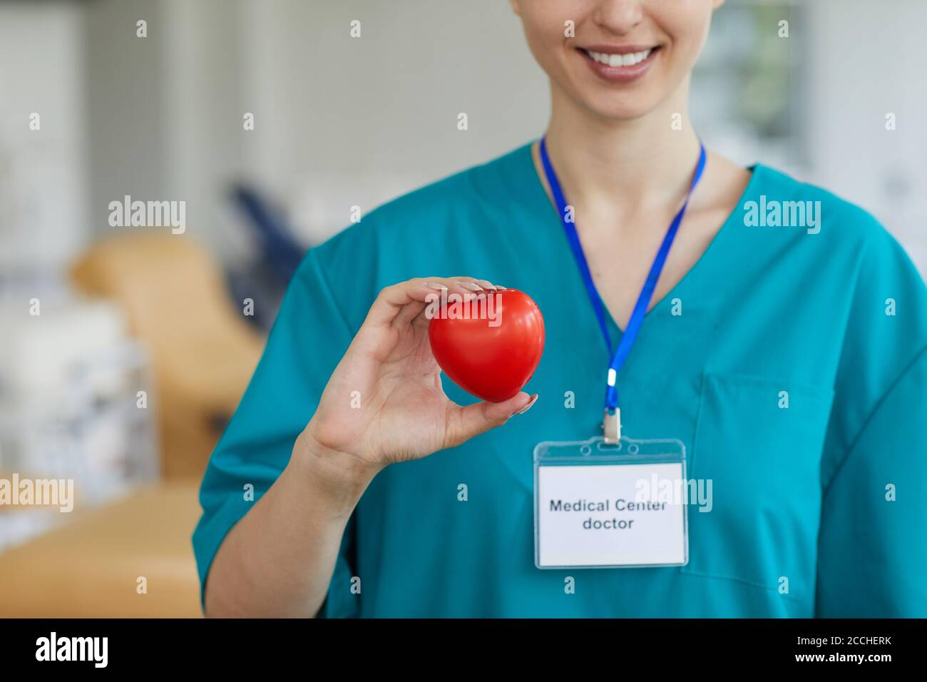 Primo piano del medico cardio femminile in forma di cuore di tenuta uniforme e sorridendo mentre si sta in ospedale Foto Stock