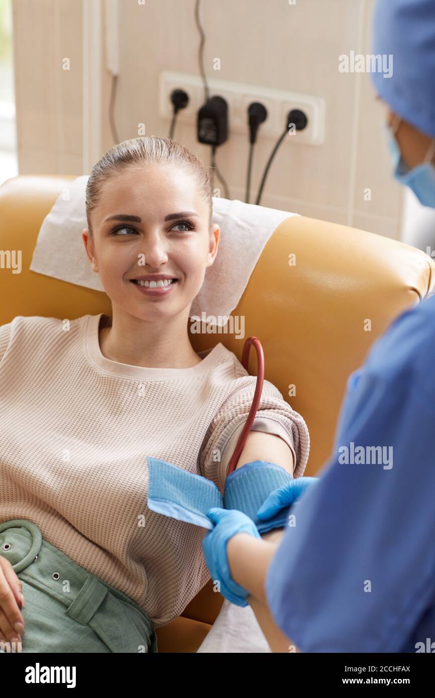 Giovane donna sdraiata sul divano e donando sangue mentre sorride al personale infermieristico Foto Stock