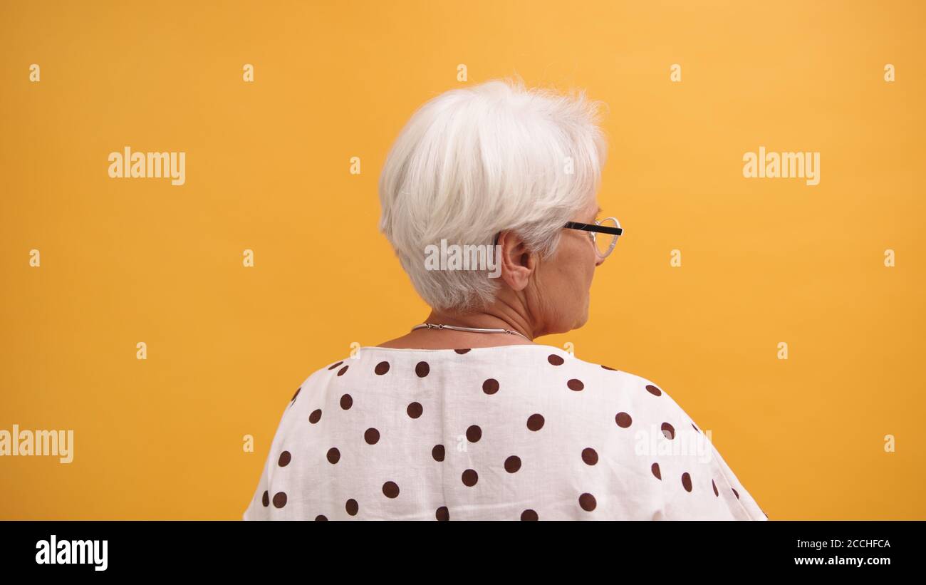 Vista posteriore di una donna senior con capelli grigi isolata sullo sfondo arancione. Foto di alta qualità Foto Stock