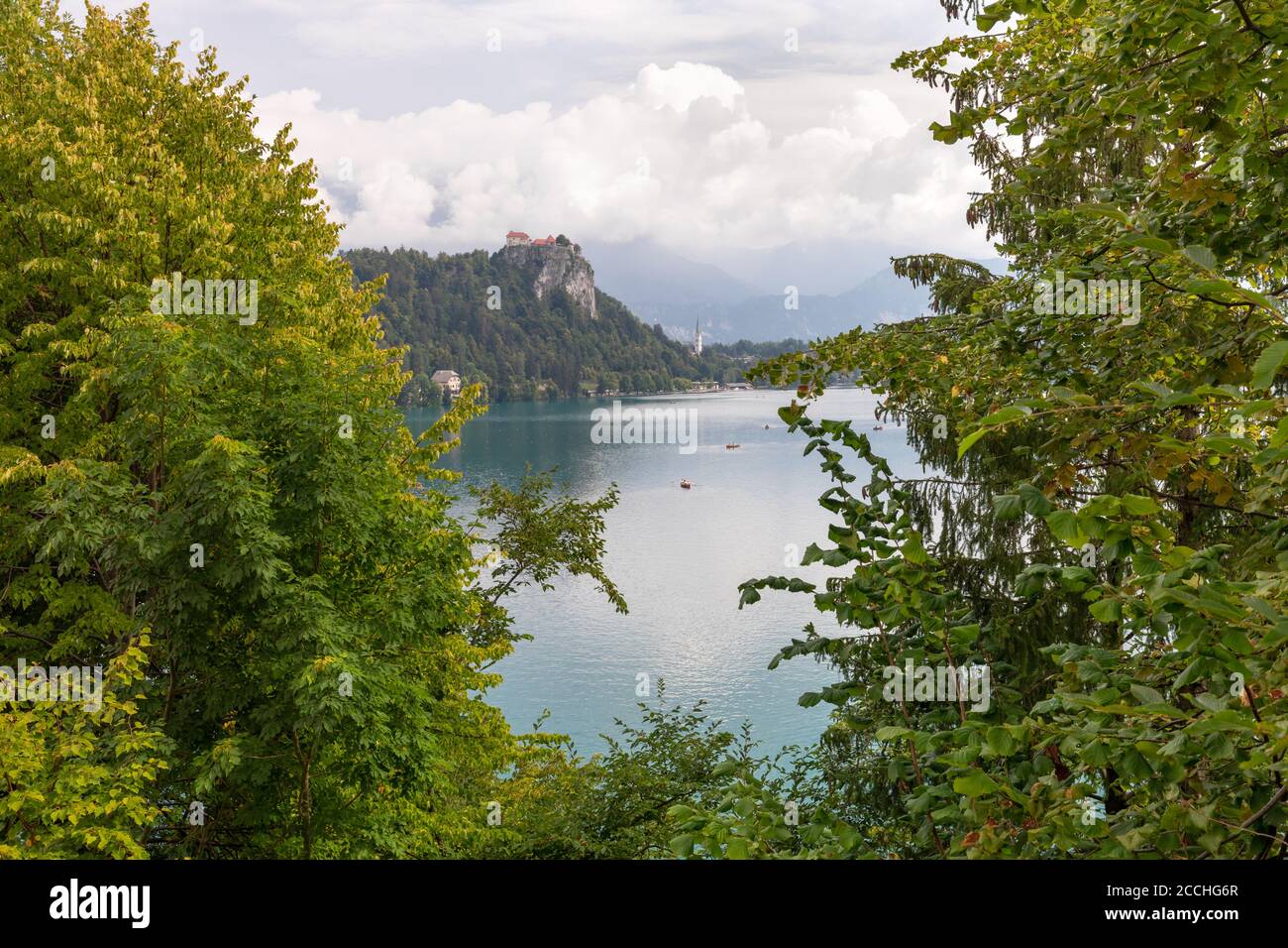 Iconico paesaggio sloveno, con un lontano castello accoccolato su un promontorio che si affaccia sul lago Bled, incorniciato da vegetazione verde Foto Stock