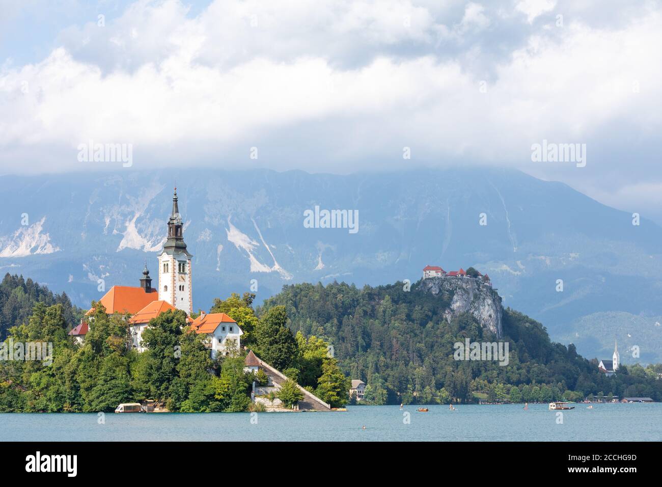 Primo piano dell'iconica isola slovena sul lago Bled, circondato da alberi e vegetazione, sotto un cielo estivo blu con nuvole soffici Foto Stock