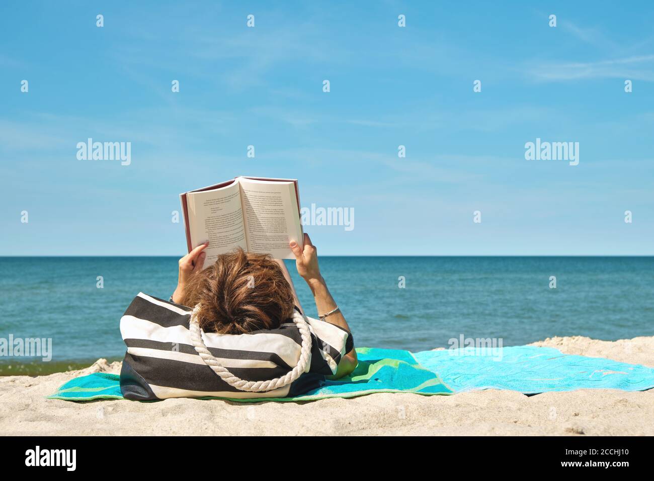 Donna caucasica sdraiata sulla spiaggia che legge un libro su giorno estivo luminoso Foto Stock