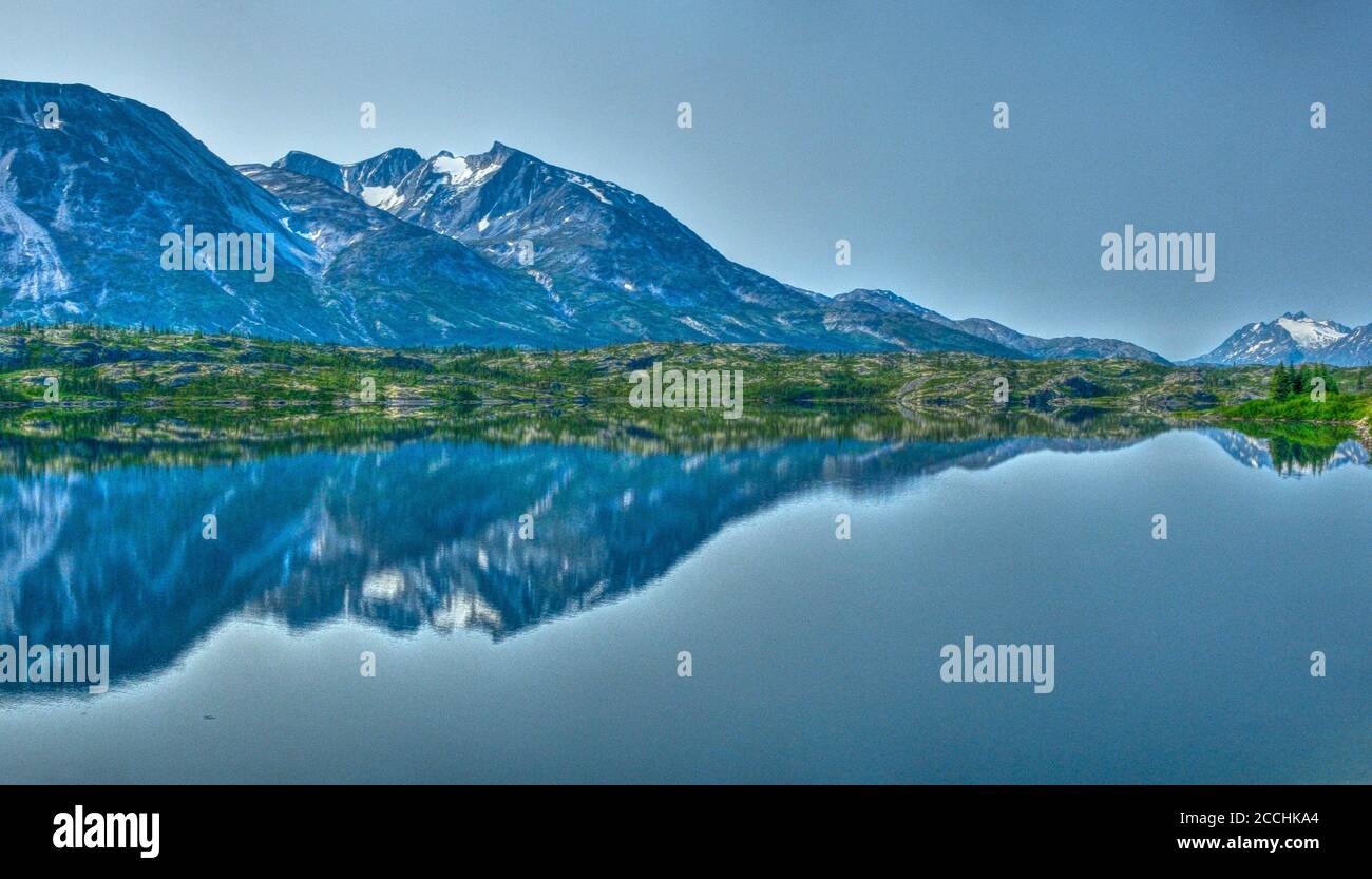 L'immagine è stata scattata a Yukon, Canada, che cattura l'aspra catena montuosa in una chiara giornata di sole che si riflette in acque calme e ferme. Foto Stock