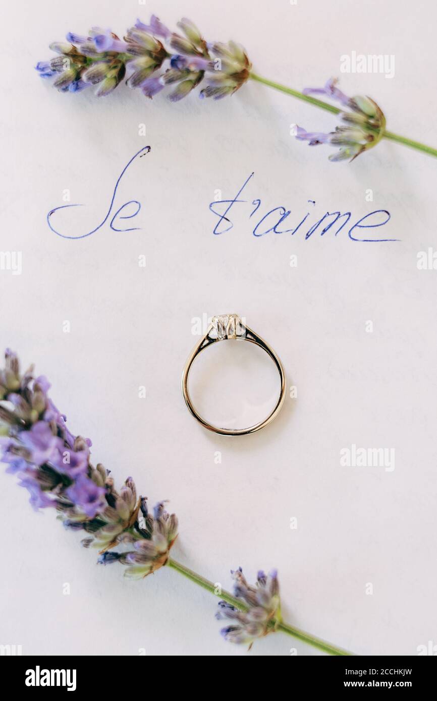 L'anello di nozze della sposa con una gemma su un foglio bianco con l'iscrizione JE t'aime e lavanda. Foto Stock