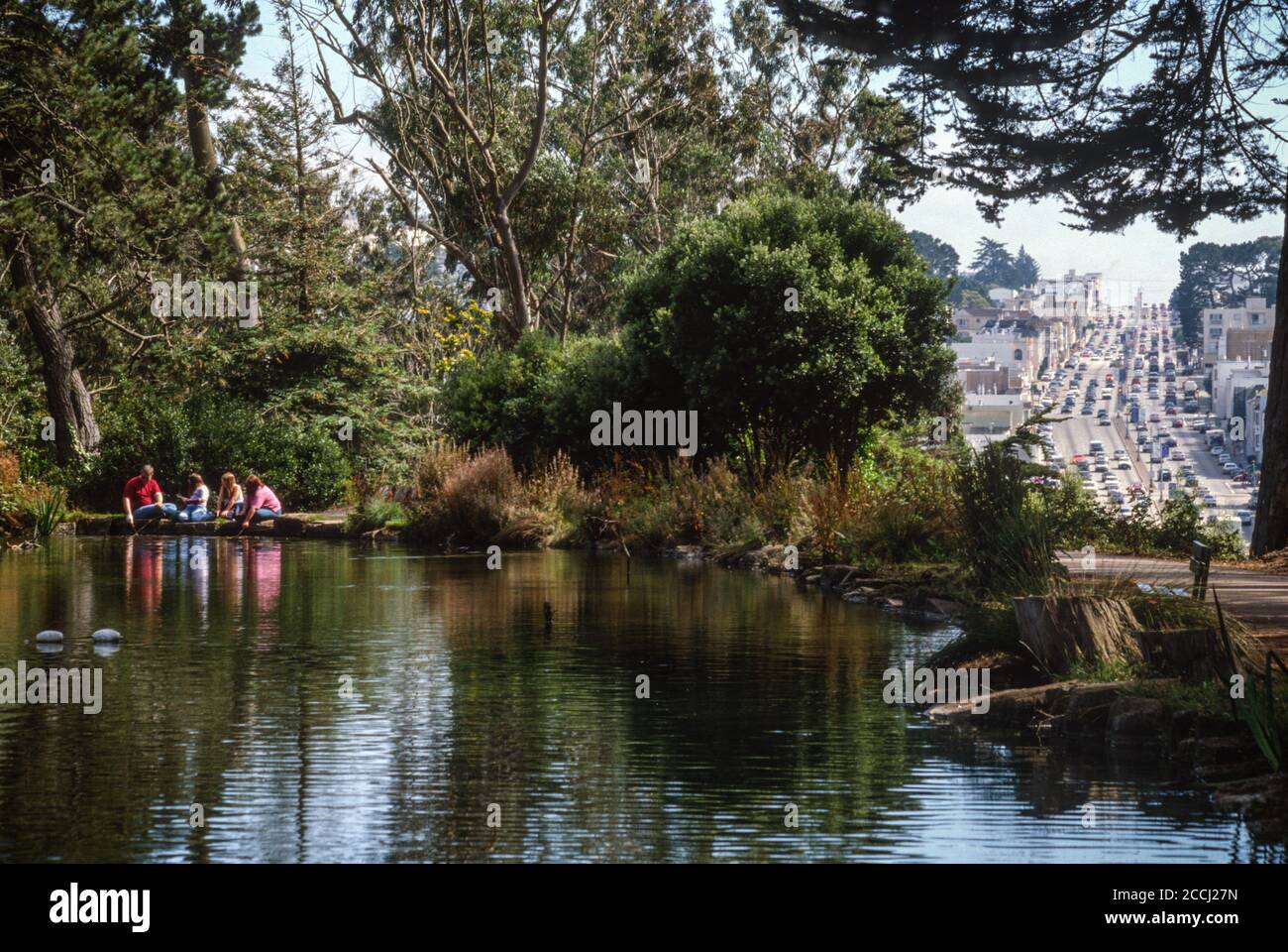 San Francisco, California, Stati Uniti. La famiglia che alimenta i pesci al lago Stow, Golden Gate Park. 19th Avenue Traffic sulla destra. Foto Stock