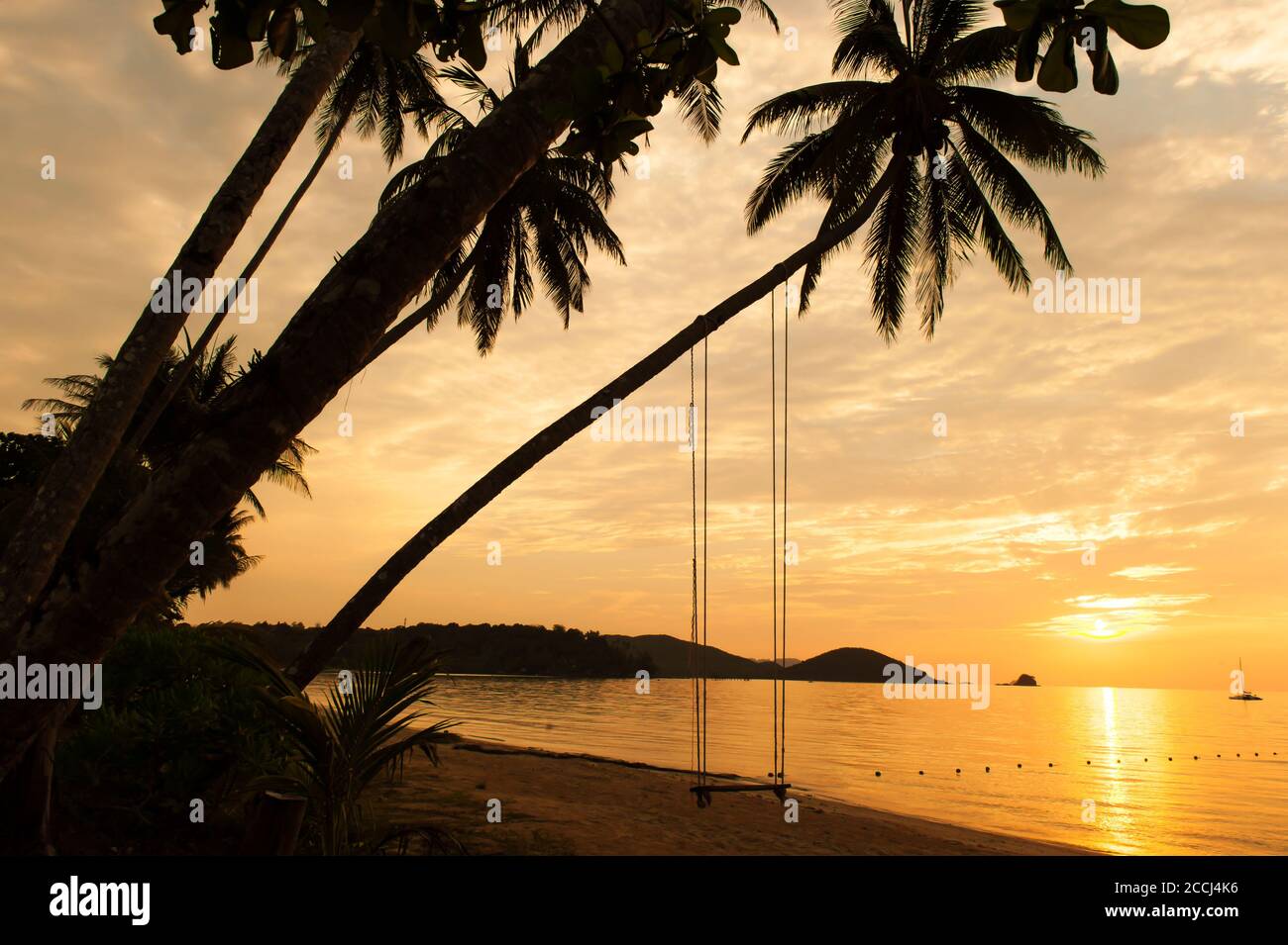 Tranquilla isola tropicale al tramonto d'estate, silhouette di palme da cocco e altalena contro il suggestivo cielo del tramonto. Isola di Koh Mak, Thailandia. Foto Stock