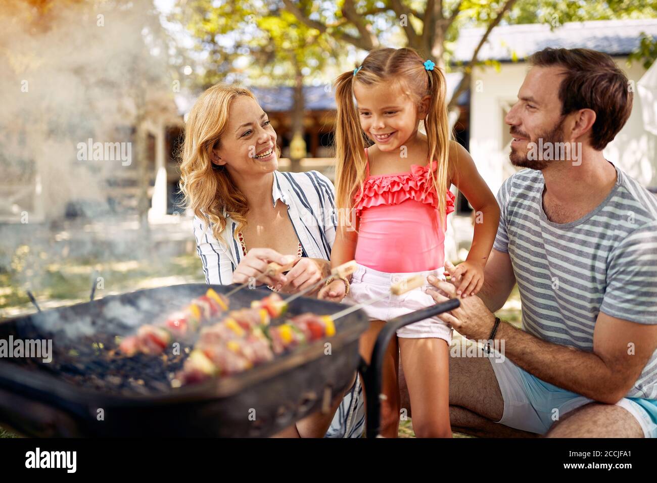 La famiglia con i suoi figli sorridenti prepara il fuoco per il barbecue di famiglia. Foto Stock