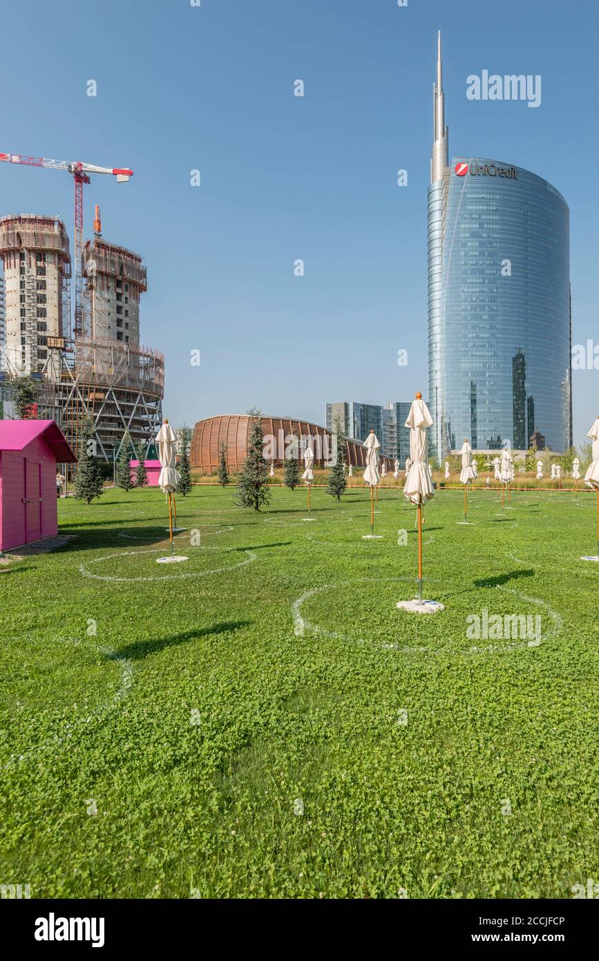 MILANO, ITALIA - Agosto 20 2020: Paesaggio urbano con ombrelloni da spiaggia su terreno prendisole su erba al centro di affari sviluppo urbano di rinnovamento, girato il mese di agosto Foto Stock