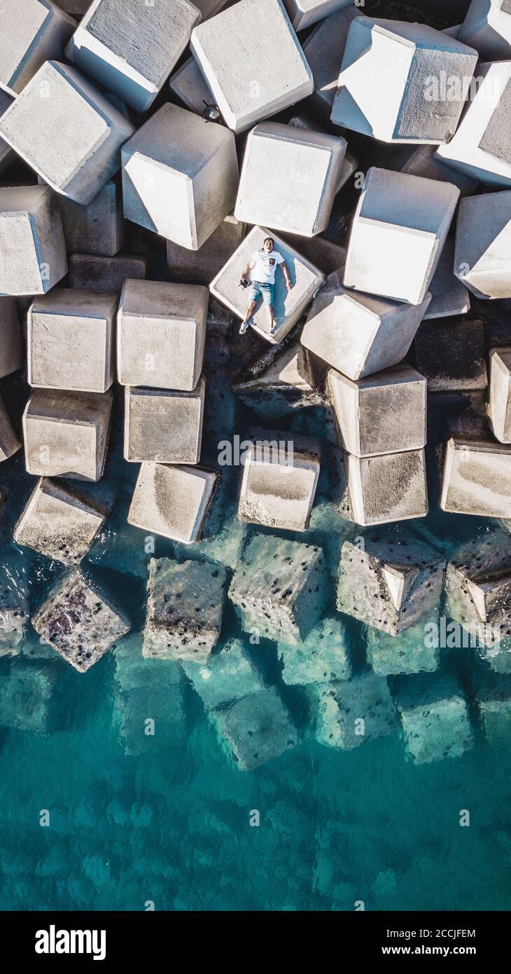 Veduta aerea di un giovane uomo su un cubo di cemento che protegge la riva dalle onde nel porto di Malaga, Spagna. Foto Stock