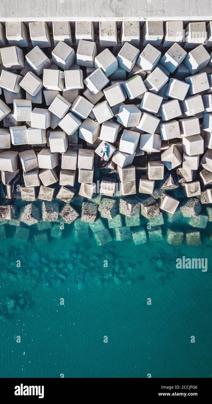 Veduta aerea di un giovane uomo su un cubo di cemento che protegge la riva dalle onde nel porto di Malaga, Spagna. Foto Stock