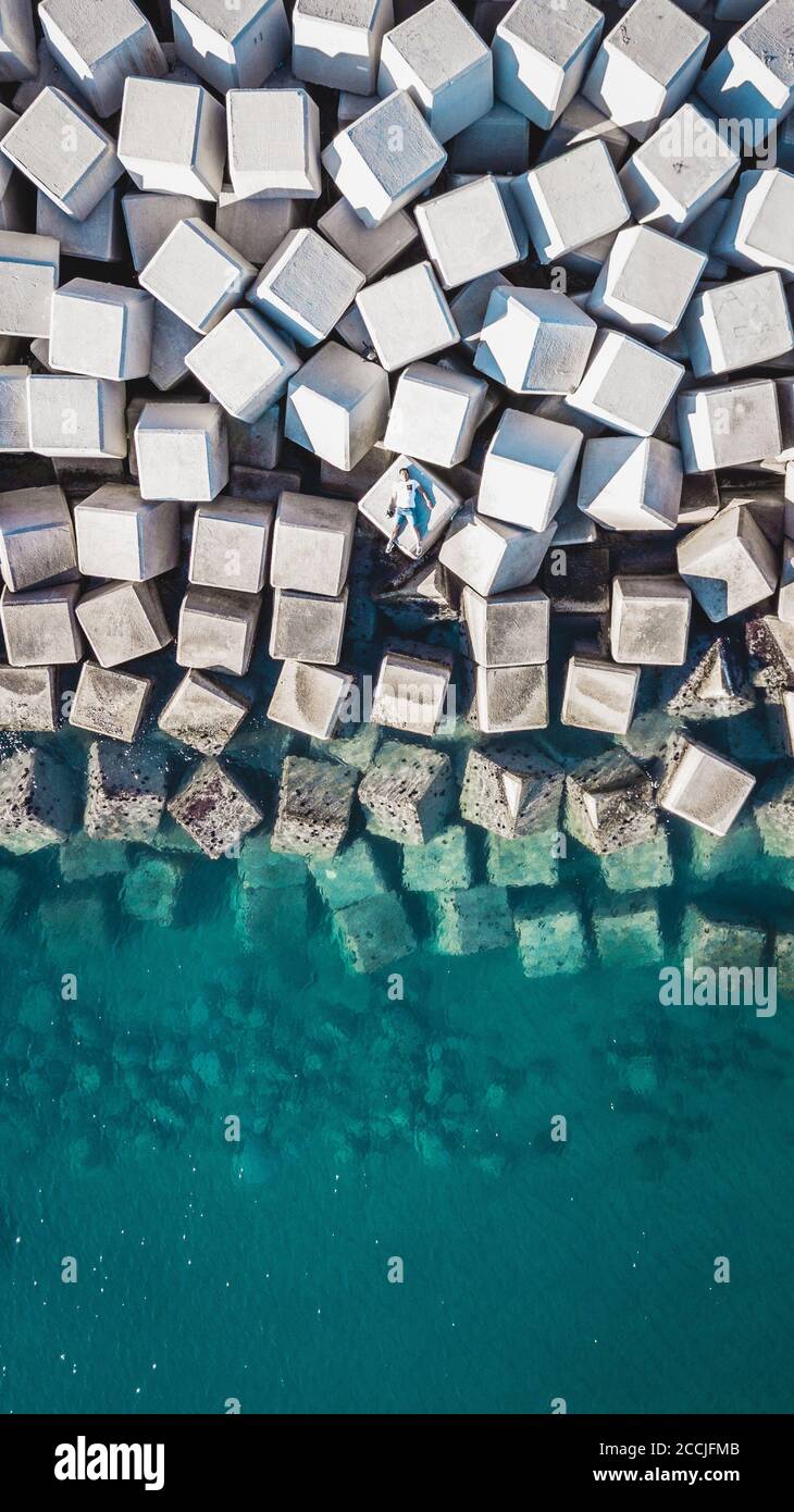 Veduta aerea di un giovane uomo su un cubo di cemento che protegge la riva dalle onde nel porto di Malaga, Spagna. Foto Stock