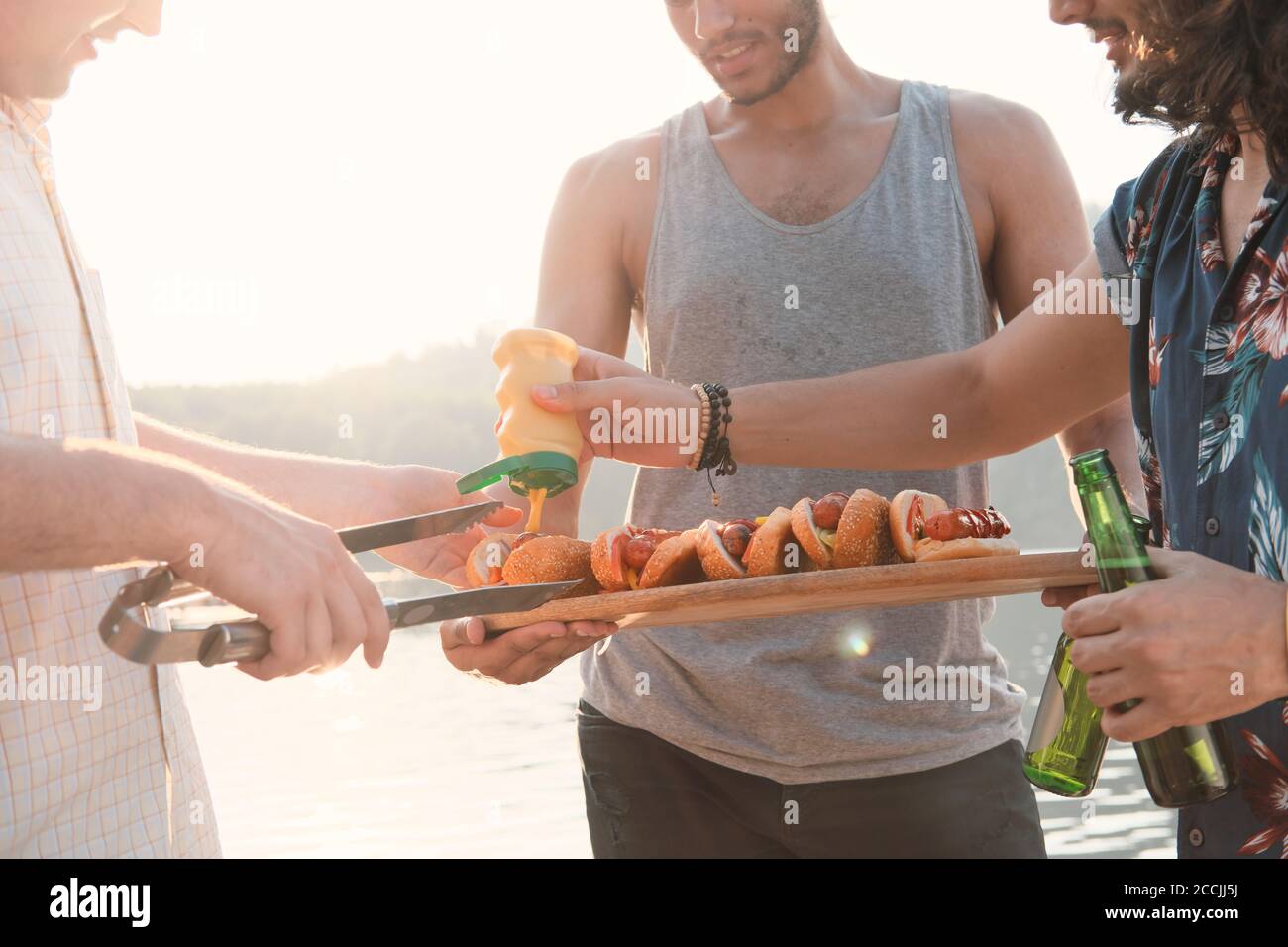 Primo piano di giovani uomini che preparano hot dog con salsa durante la festa all'aperto Foto Stock