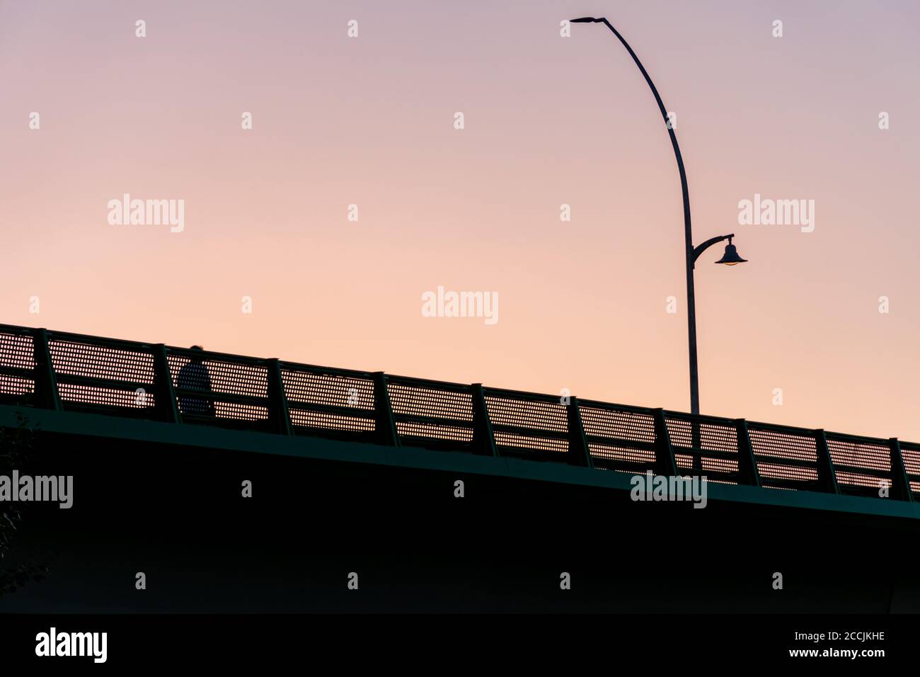 Uomo che cammina da solo su un ponte e accanto a un lampione. Foto Stock