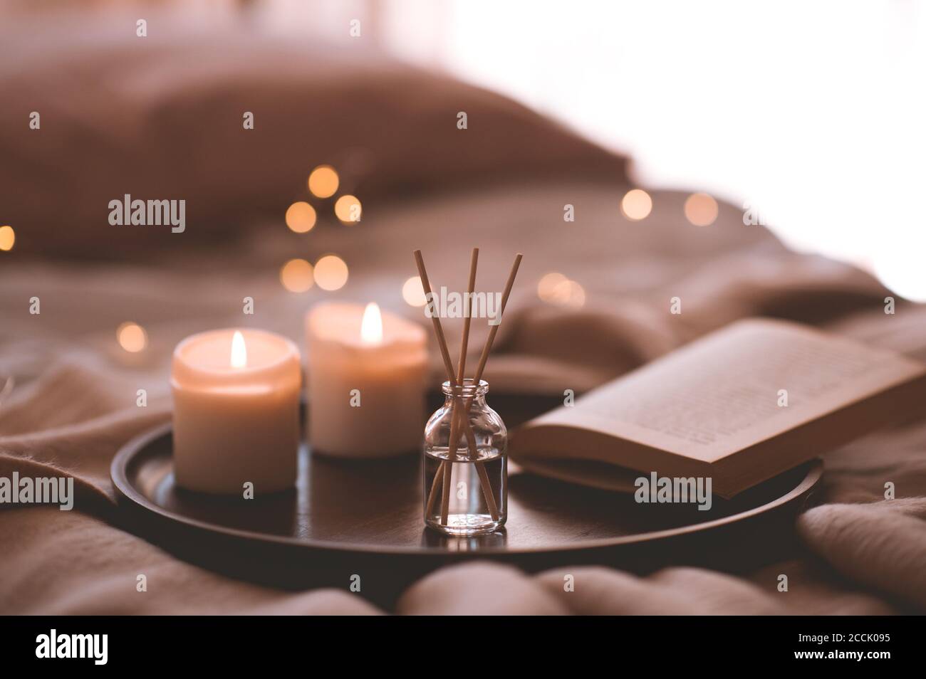 Bastoni di bambù in bottiglia con candele profumate e libro aperto su vassoio di legno in primo piano letto. Aroma domestico. Foto Stock