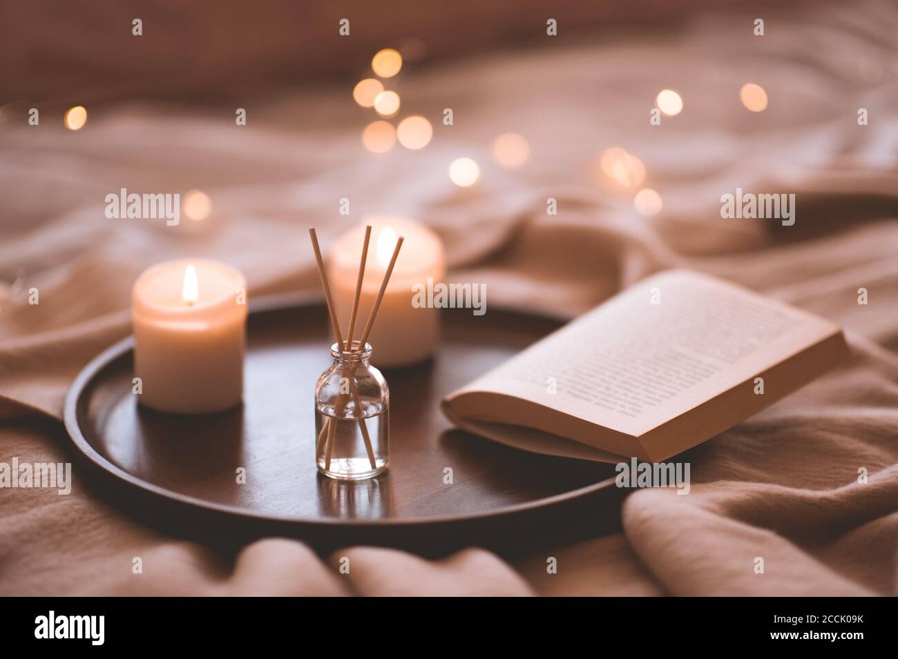 Bastoni di bambù in bottiglia con candele profumate e libro aperto su vassoio di legno in primo piano letto. Aroma domestico. Foto Stock
