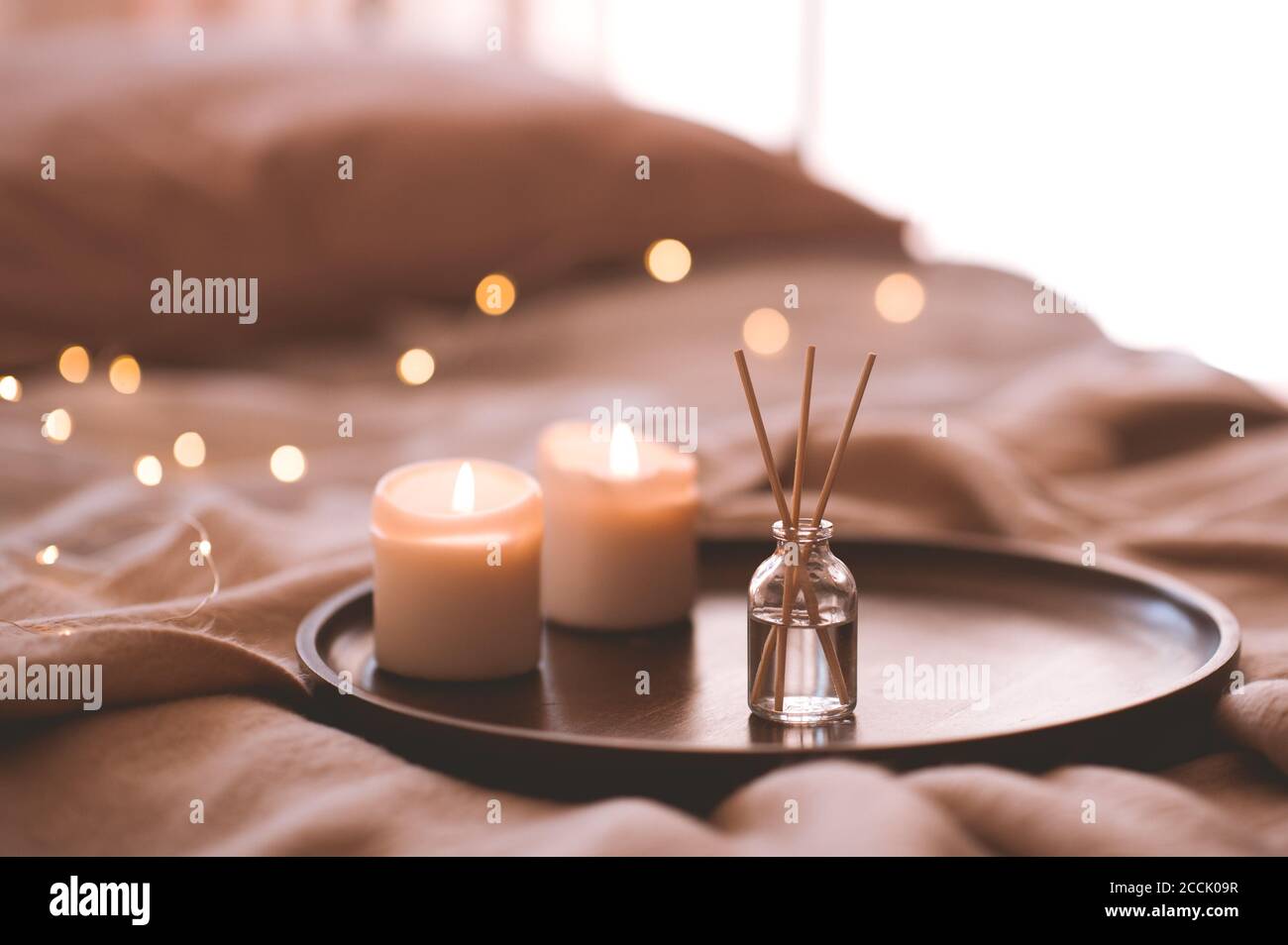 Aroma bastoni di bambù in bottiglia con liquido profumato con candele che rimangono su vassoio di legno in primo piano letto. Foto Stock