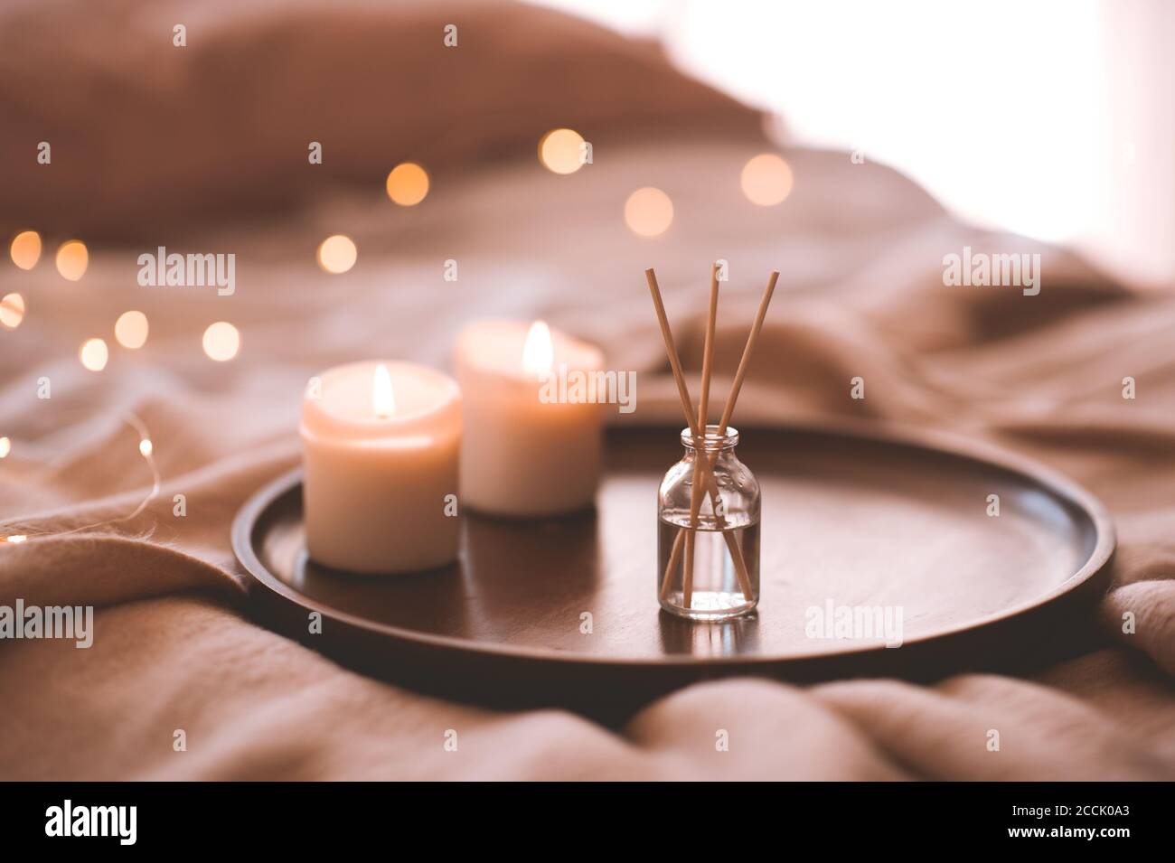 Aroma bastoni di bambù in bottiglia con liquido profumato con candele che rimangono su vassoio di legno in primo piano letto. Foto Stock