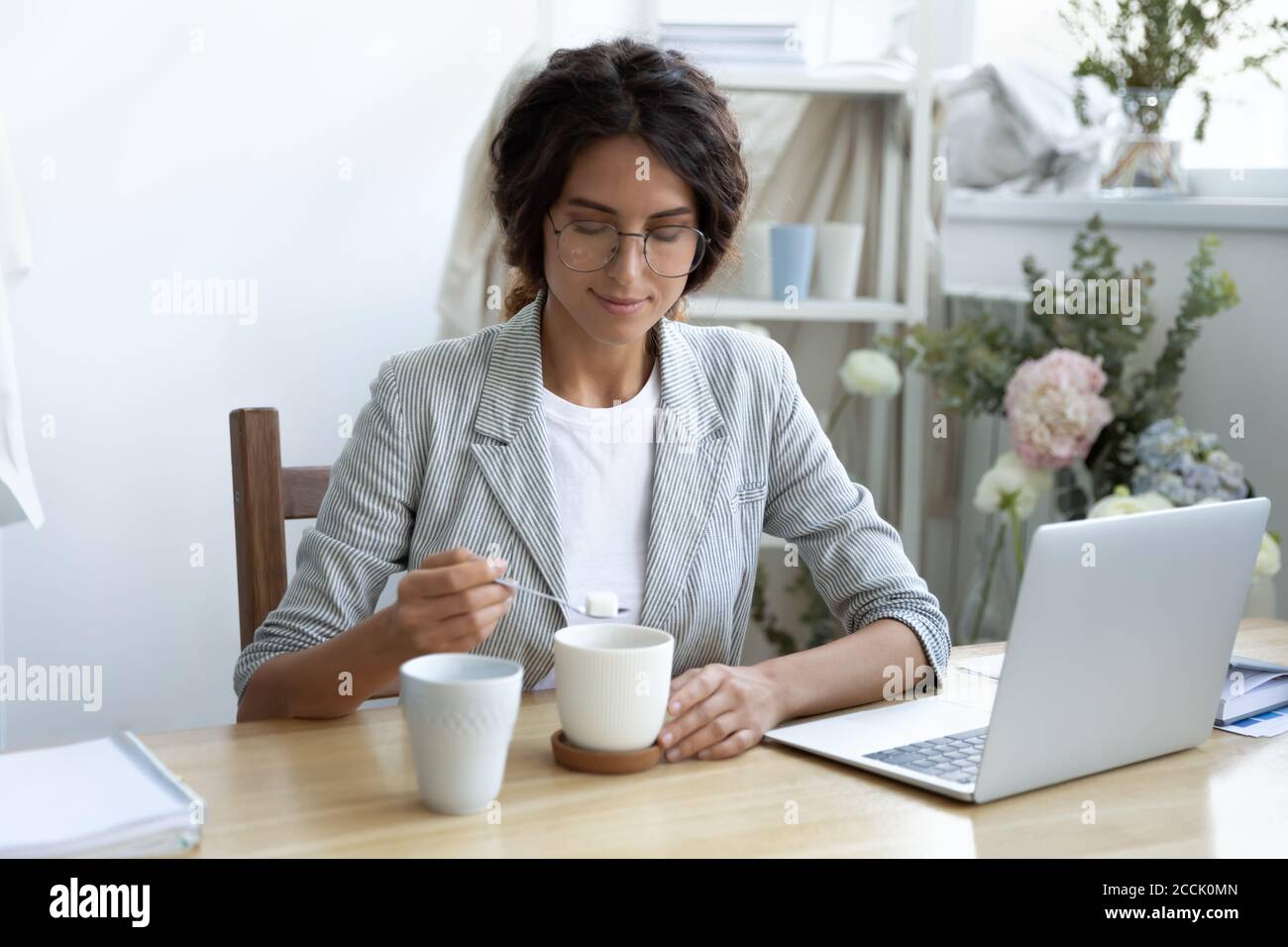 Felice giovane donna d'affari aggiungendo zucchero raffinato alla tazza di caffè. Foto Stock