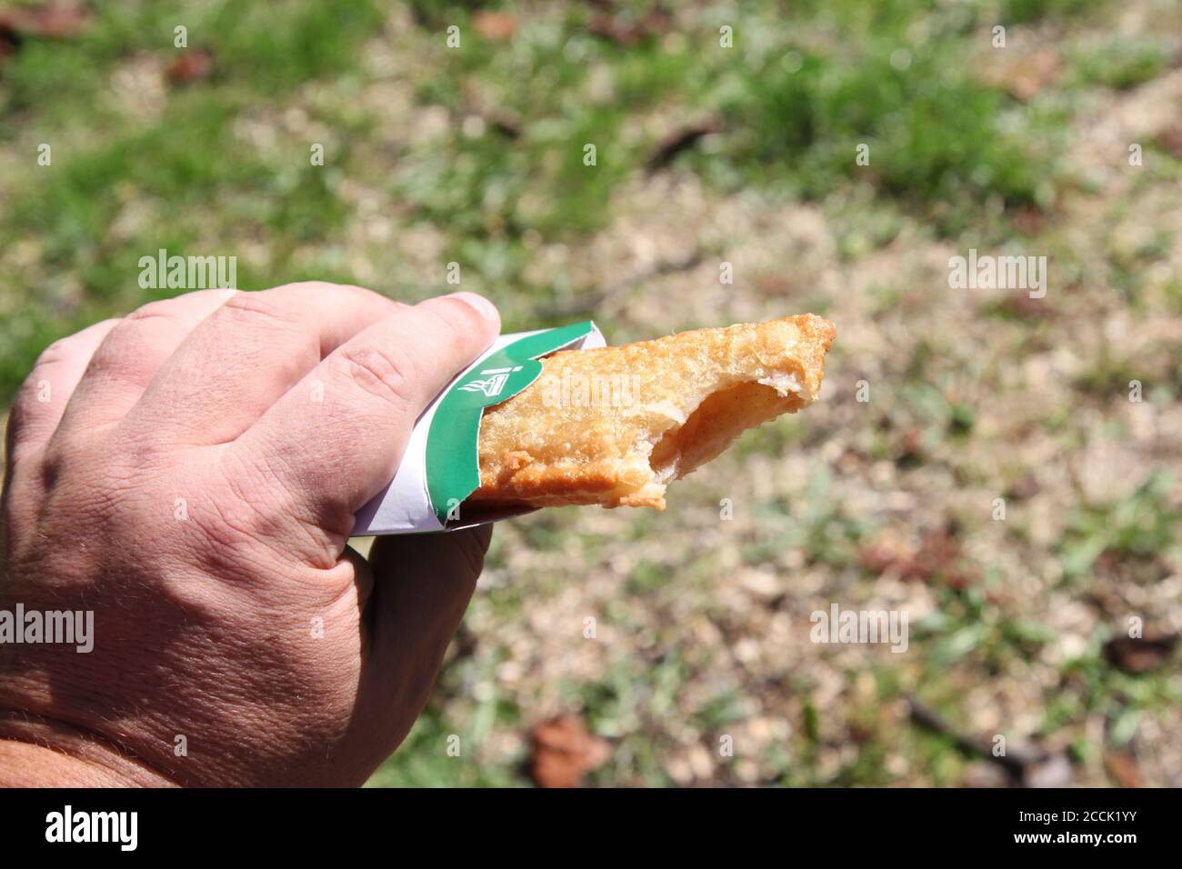 Un uomo prende un morso da una torta calda di mele di McDonald, tenuto in mano, all'aperto, giorno di sole, 2020 Foto Stock
