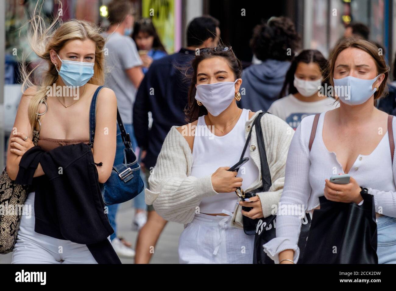 Giovani donne che indossano copriviso in una strada trafficata, Londra, Regno Unito Foto Stock