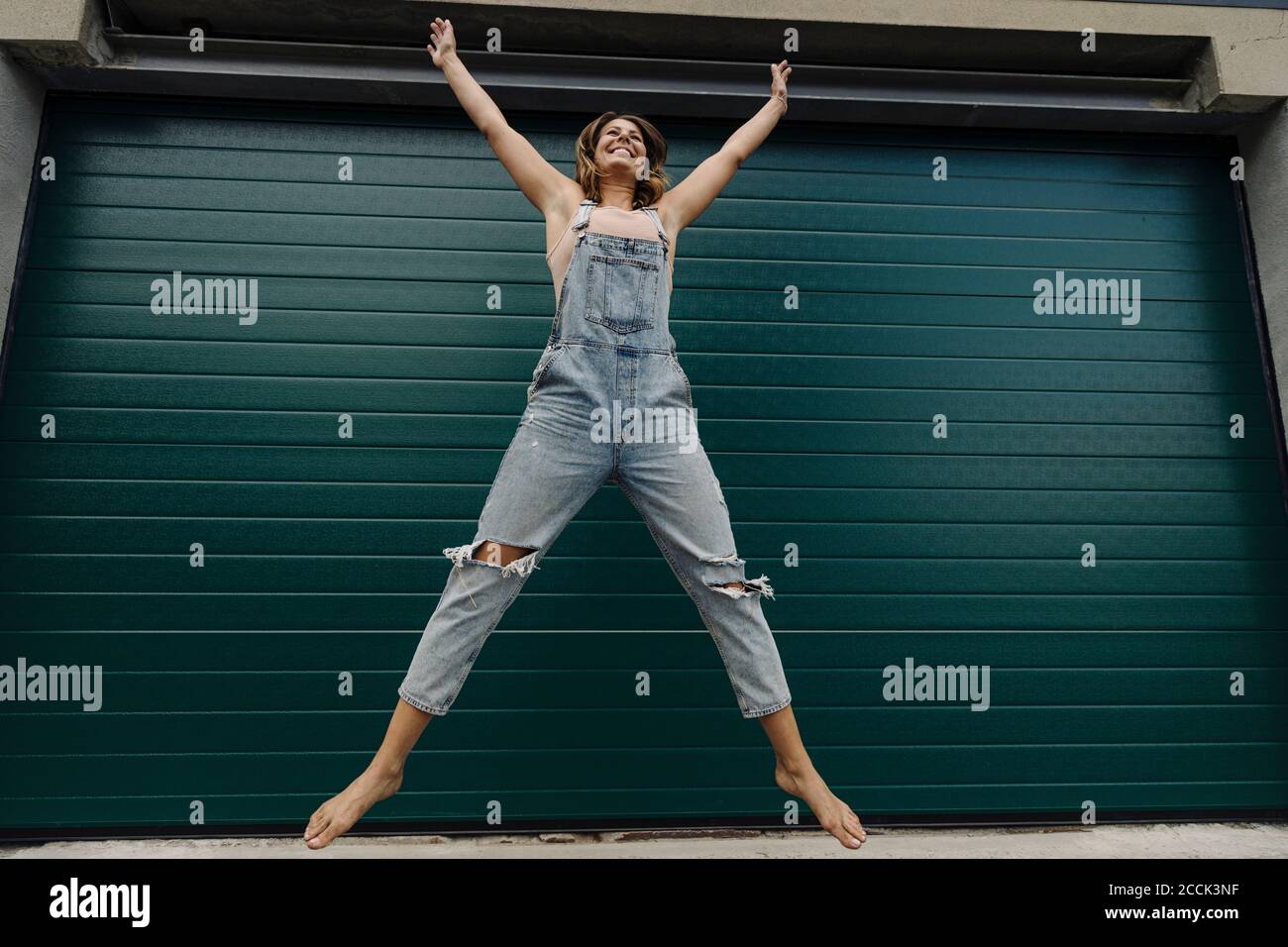 Giovane donna spensierata che salta di fronte alla porta del garage Foto Stock