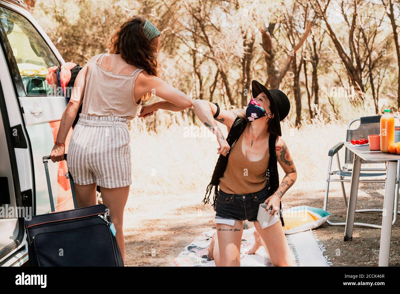 Donne con maschere protettive salutano con ellbow durante il camper viaggio Foto Stock