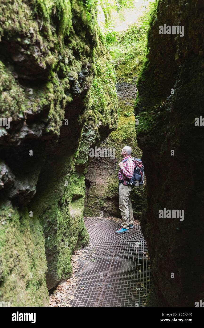 Anziano escursionista maschile in piedi tra formazioni rocciose nella foresta di Turingia, Germania Foto Stock
