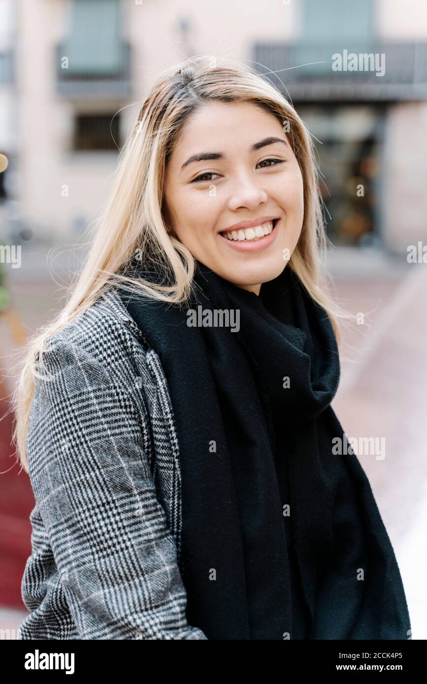 Giovane donna sorridente che guarda la macchina fotografica in città Foto Stock